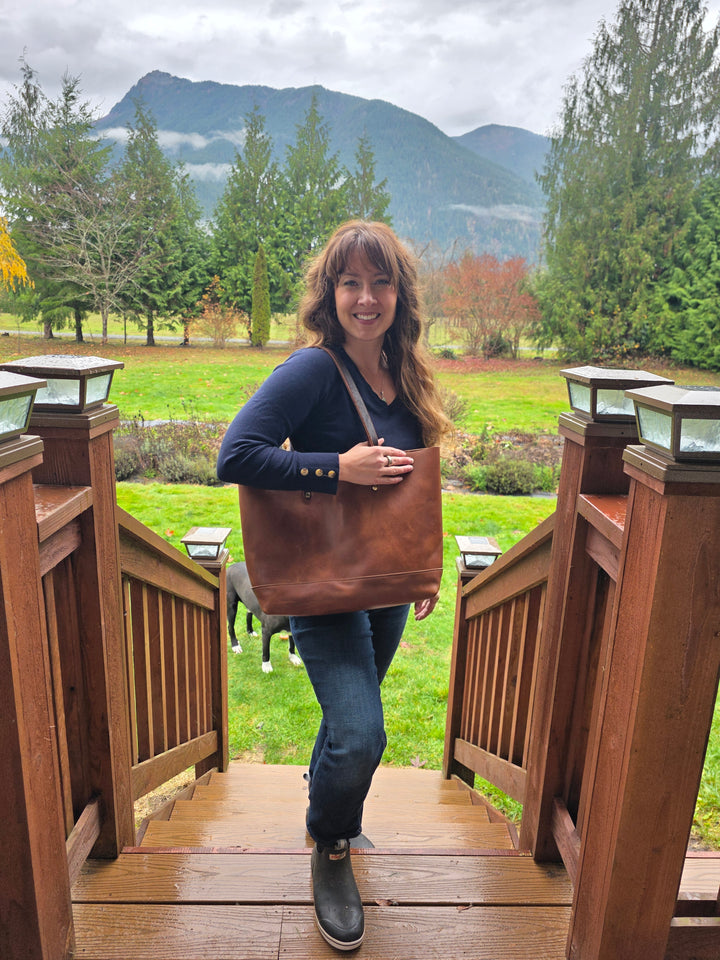 Person holding a brown leather bag outdoors with mountains in the background #color_brown