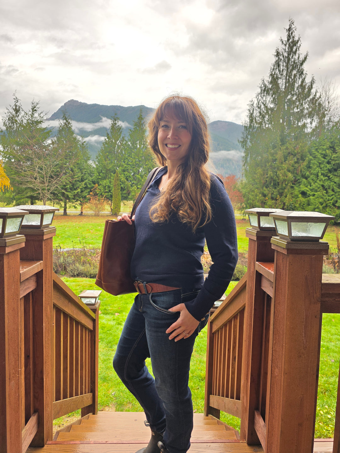 Person standing on a wooden deck with a scenic view of trees and mountains. #color_brown