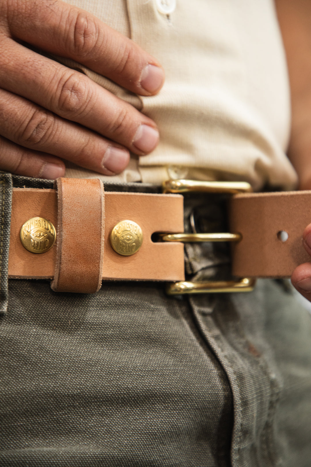 Russet horsehide belt lifestyle green pants holding strap end zoomed in