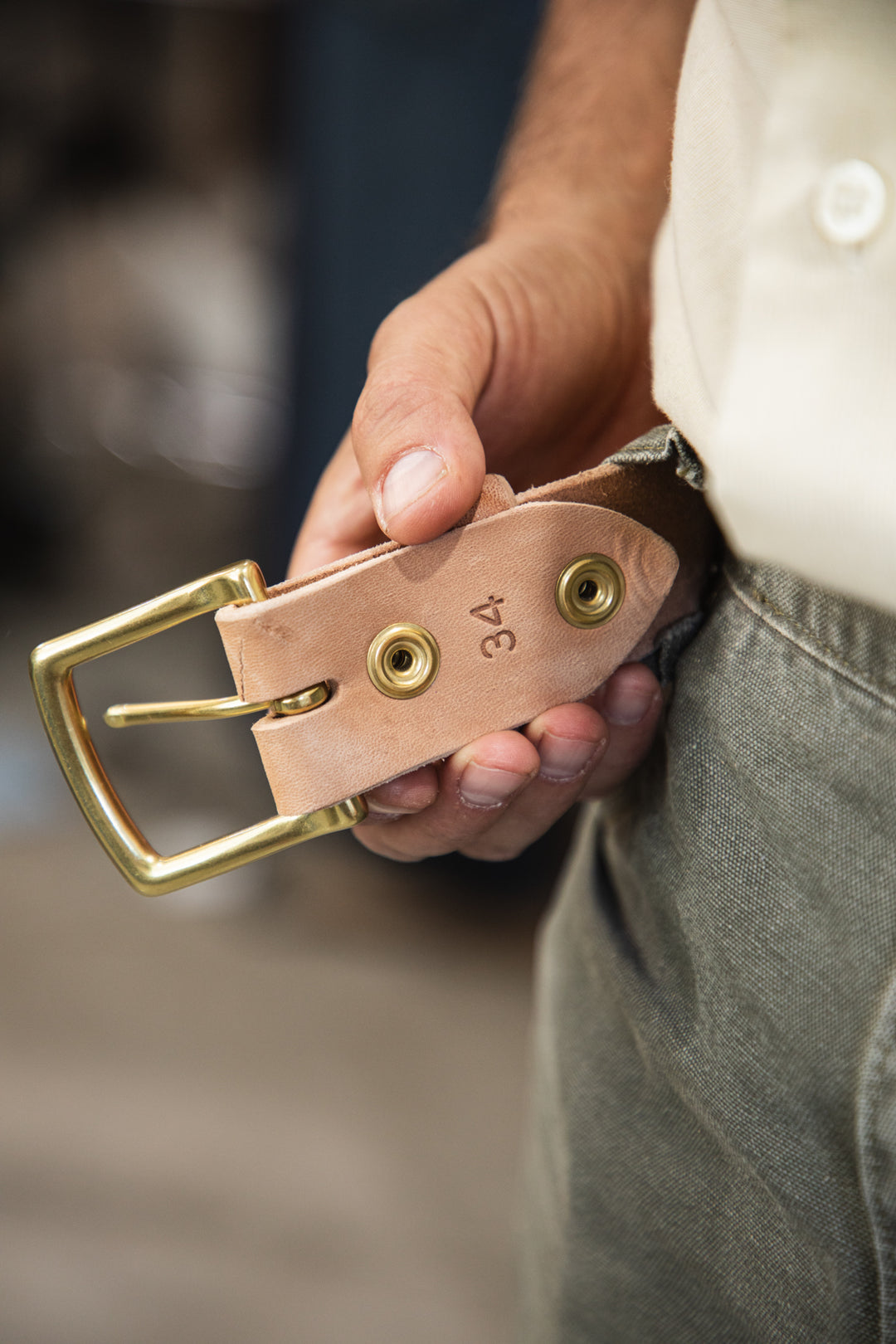 Russet horsehide belt lifestyle green pants holding buckle end showing belt size