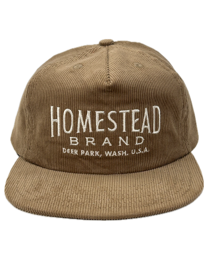 Tan colored baseball hat with “homestead brand deer park wash.” Embroidered on the front on top of a white background