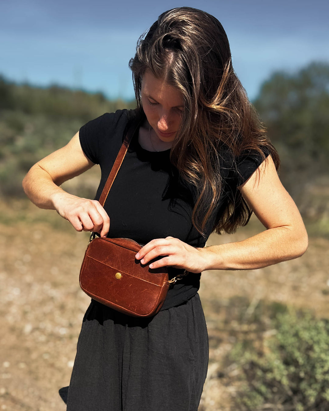 Woman holding a brown leather bag outdoors with a natural background #color_brown