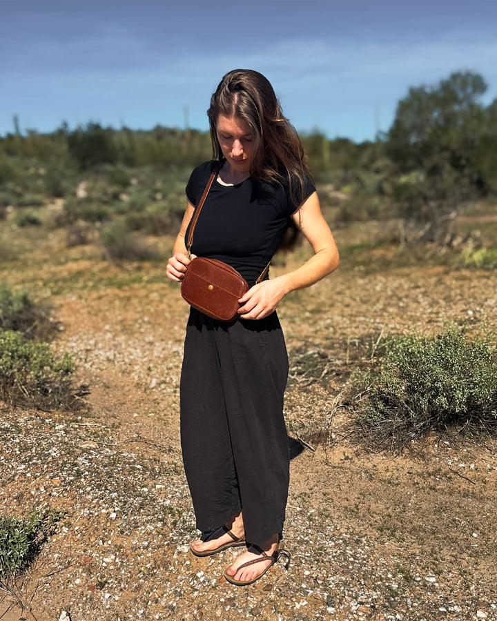 Woman holding a brown leather bag in a desert-like setting #color_brown