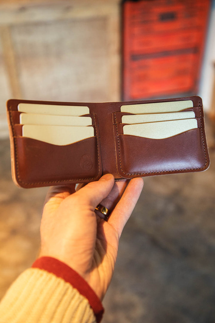 Brown leather wallet with cream interior held by a hand against a blurred background #color_brown