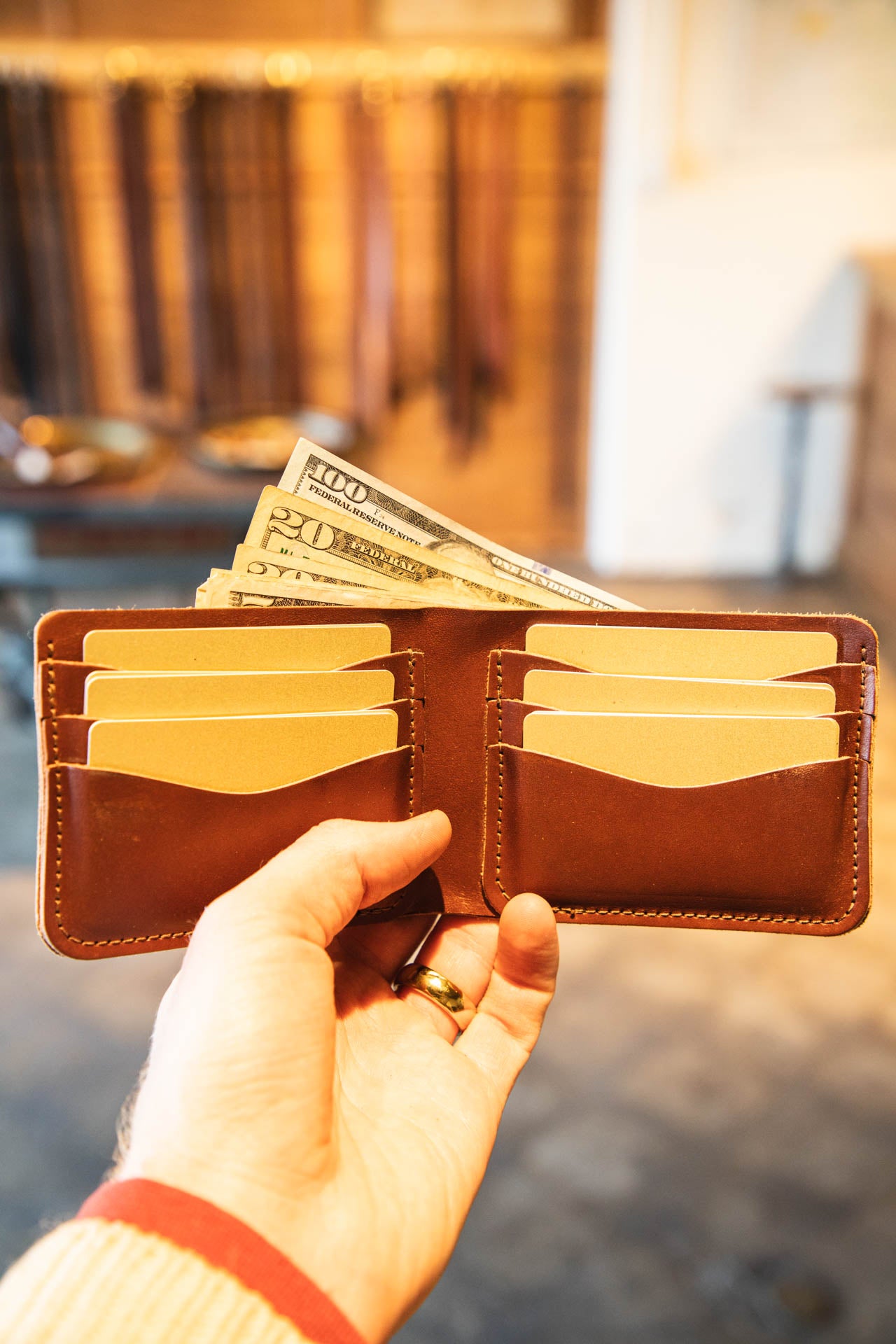 Hand holding a brown wallet with money and cards against a blurred indoor background #color_brown
