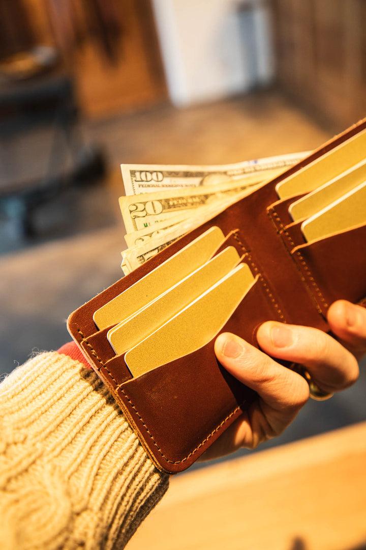 Brown leather wallet with money and cards held by a person wearing a beige sweater #color_brown