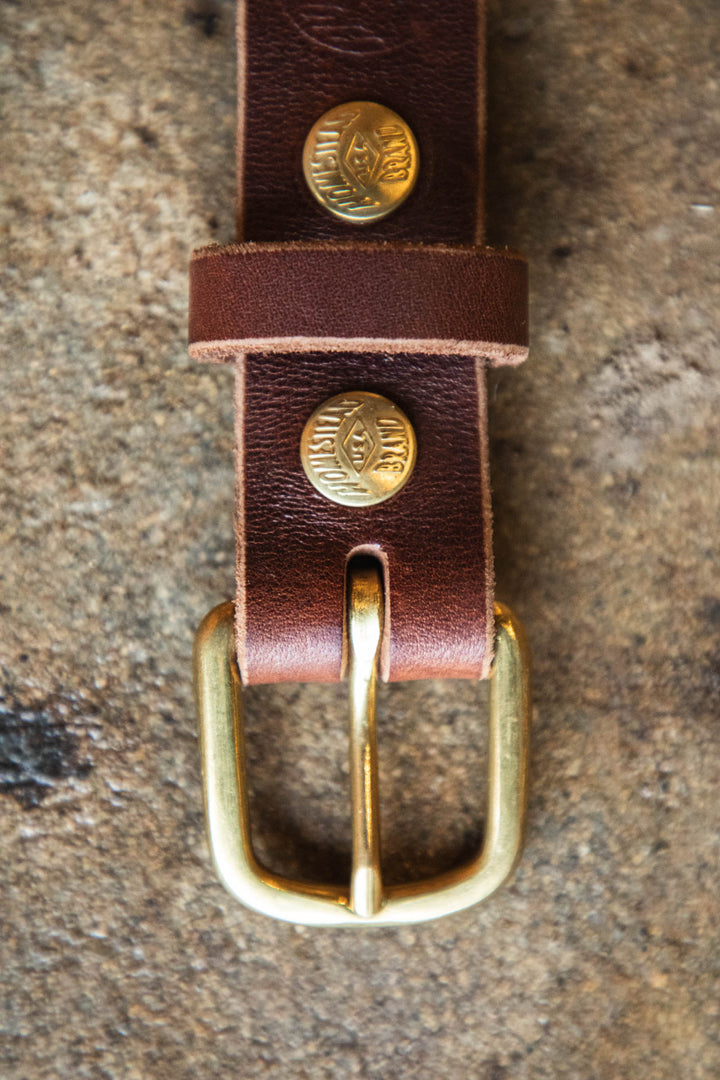 Brown leather belt with brass buckle on a textured surface #color_brown
