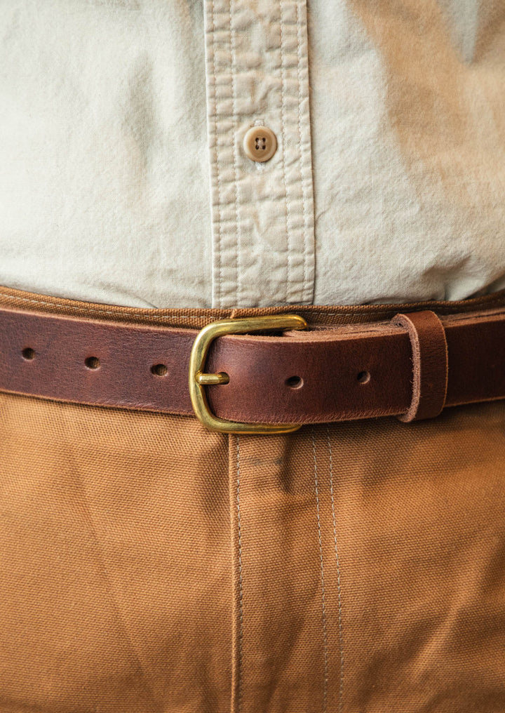 Close-up of a person wearing a beige shirt and brown pants with a leather belt. #color_brown