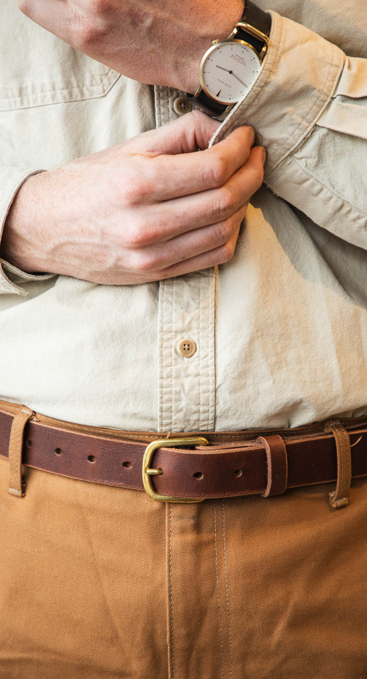 Person adjusting a button on a beige shirt with a brown belt #color_brown